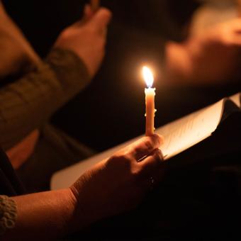A person holds a glowing, burning candle on their hand during a vigil service at Trinity Church