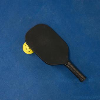 Pickleball racquet and ball on a blue court.