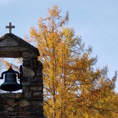 Chapel's cross and bell are framed by yellow leaves under a blue sky
