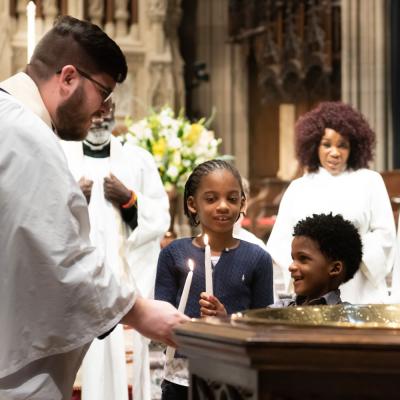 The Rev. Matthew A. Welsch, Priest for Youth and Family, and two young parishioners hold candles near the baptismal font in the chancel of Trinity Church