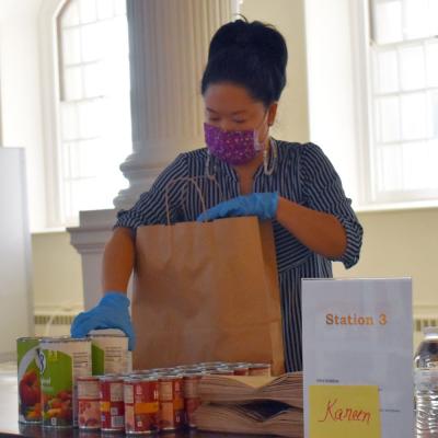 Trinity staff member packs a brown bag with canned goods at the Compassion Market
