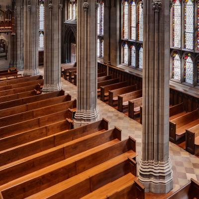 An overhead shot of wooden pews in Trinity Church lining a large wall of stained glass windows with light shining through