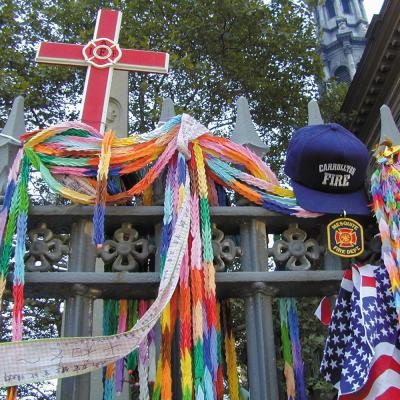 Flags, garlands, hats, a cross, and other memorial items hung on the fence surrounding St. Paul's Chapel