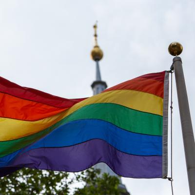 Pride flag hoisted in front of St. Paul's Chapel, with the steeple in the background.