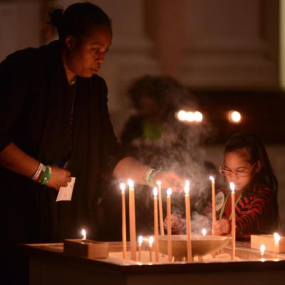 A woman lights a tall, thin candle during a community prayer service