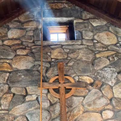 Beam of light coming in through a small window in a stone wall of the Retreat Center chapel, above a wooden cross