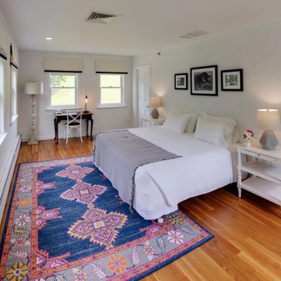 A guest room in the Main House, with a king-sized bed, blue, pink and orange rug, nightstand, fresh flowers, and a desk