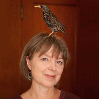 Portrait of Lyanda Lynn Haupt with a bird standing on her head.