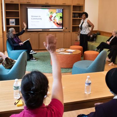 Women raise hands in a Commons classroom, responding to the discussion leader. 