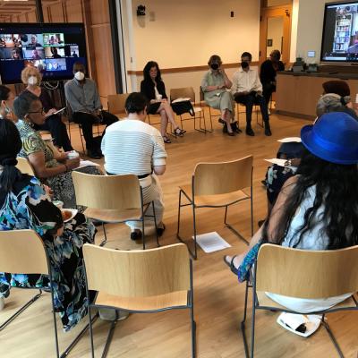 Adults sit in a semi-circle to discuss St. Paul. There are two television screens in the background for online participants to contribute to the discussion.