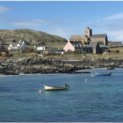 Coast of Iona with two fishing dinghies tied in the shallow water with Bishops House and the Iona Abbey in the background