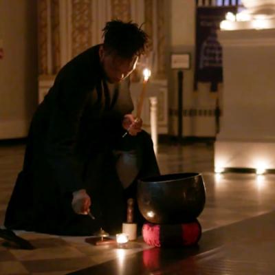 Man in a black coat kneels in a dimly-lit St. Paul's Chapel to light a candle.