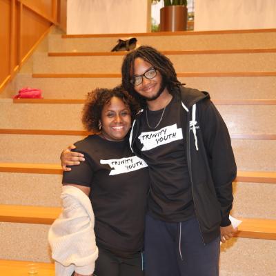 Trinity Youth staff Jayla Allen and participant smile by the staircase at the Trinity Commons lower level lobby.