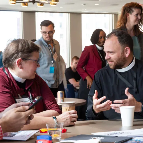 Two priests talk to one another while seated at a table.