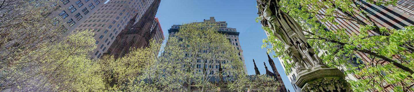 Springtime image of Trinity Church with buildings in background and Astor Cross, looking up at the sky