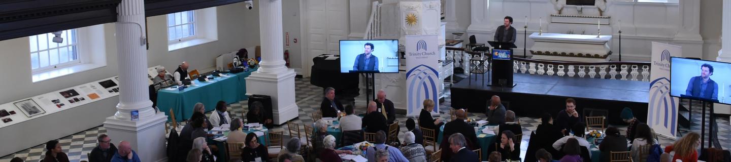 A photo from Trinity Institute shows a speaker at the front of St. Paul's Chapel and people gathered in tables in front.