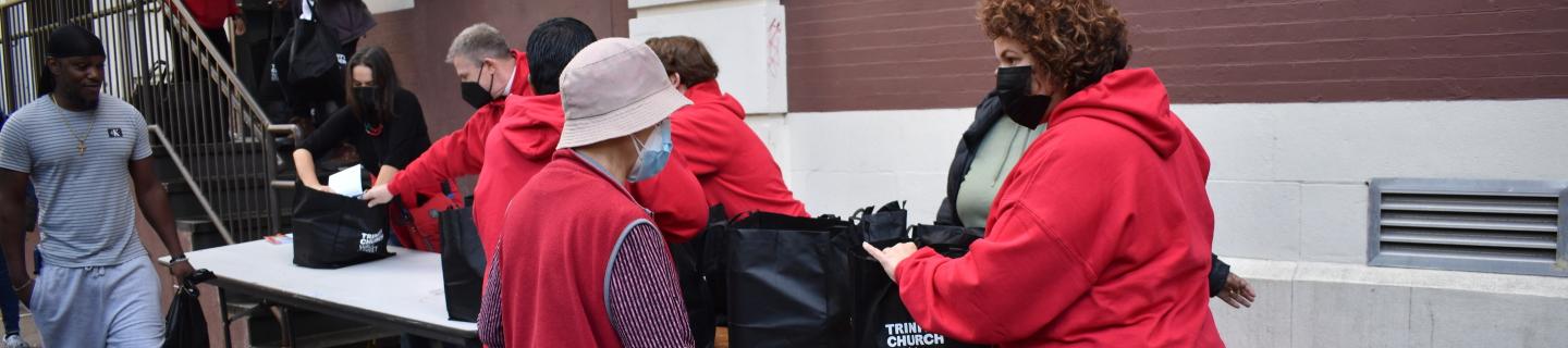 Volunteers in red hoodies distribute packed bags of groceries to community members.